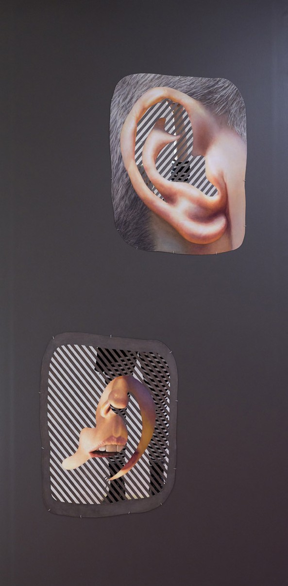 A grey wall with two cut-outs, one of an ear and one of a mouth. A performer is visible through slatted paper.
